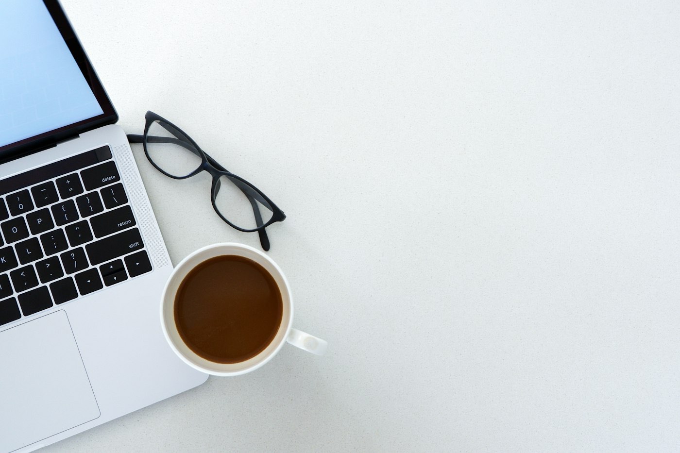 Ordinateur portable, café et lunettes sur un bureau blanc